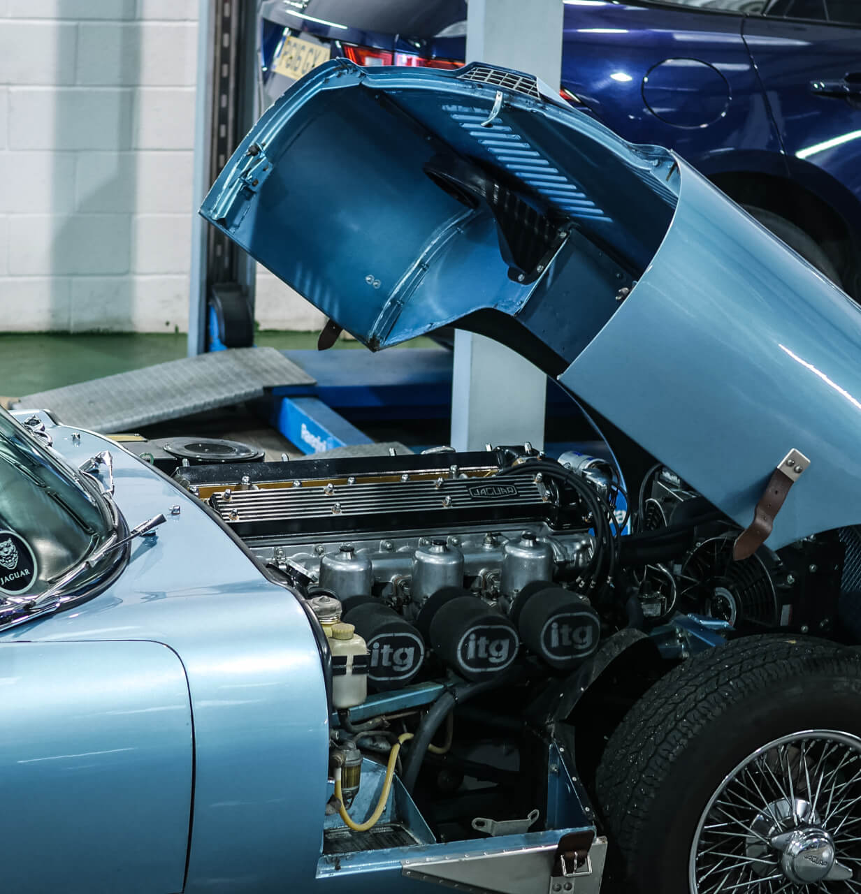 Metallic blue Jaguar E-Type in garage with hood opened exposing the engine